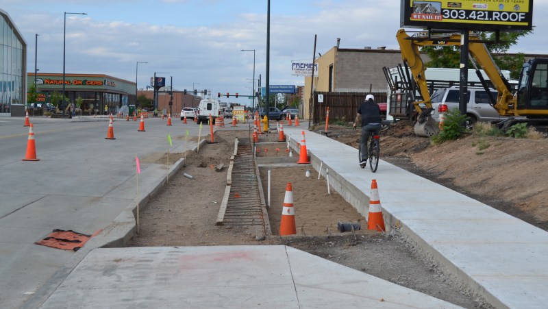 A man rides his bike on a brand new sidewalk, next to an unfinished piece of the bikeway. Photo: David Sachs