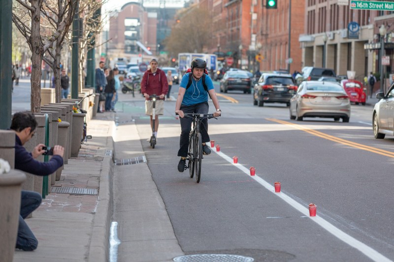 Tactical urbanism: A cyclist and scooter rider ride in the Wynkoop Street bike lane protected by red cups and tomatoes during the #RedCupProject demonstration on April 26.