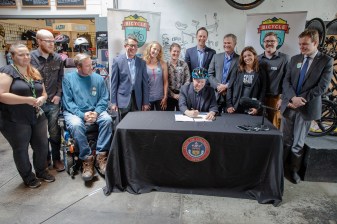 Street safety advocates watch as Gov. Jared Polis wears a bike helmet while signing a bill into law that stiffens penalties against careless drivers who seriously injure vulnerable road users.