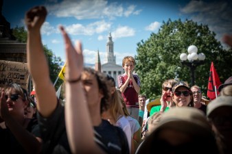 A boy looks at the demonstration while protestors hold their hands in the air. Denver City Hall is in the background. Photo: Andy Bosselman, Streetsblog Denver