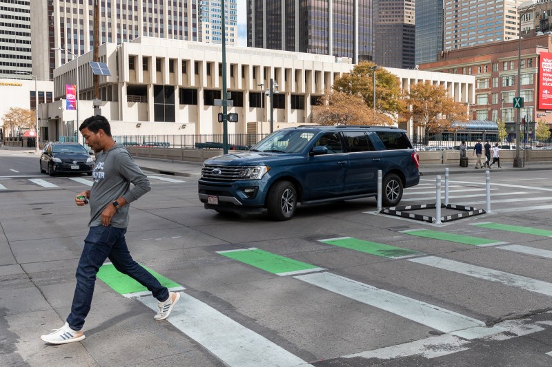 A pedestrian crosses 15th Street in Downtown Denver as a vehicle slows before turning around a newly-installed corner wedge safety treatment. Photo: Andy Bosselman